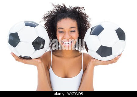 Pretty girl holding palloni da calcio e ridere per fotocamera su sfondo bianco Foto Stock
