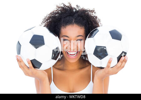 Pretty girl holding palloni da calcio e ridere per fotocamera su sfondo bianco Foto Stock