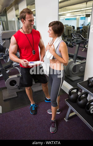 Bello personal trainer a parlare con il suo cliente in palestra Foto Stock