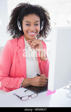 Casual graphic designer che lavora alla sua scrivania sorridente in telecamera nel suo ufficio Foto Stock