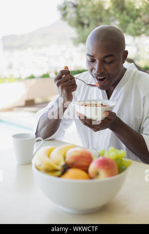 Uomo bello in accappatoio avente la prima colazione fuori in una giornata di sole Foto Stock