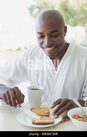 Uomo bello in accappatoio avente la prima colazione fuori in una giornata di sole Foto Stock