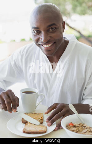 Uomo bello in accappatoio avente la prima colazione fuori in una giornata di sole Foto Stock