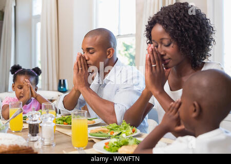 La famiglia felice dicendo grazia prima di pasto a casa in cucina Foto Stock