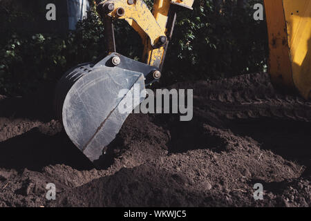 Escavatore giallo benna è di scavare un buco nel terreno nero sulla giornata di sole. Macchinari da costruzione durante il lavoro. Foto Stock