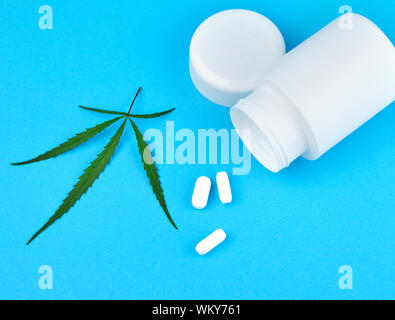 La cannabis ramo con foglie di colore verde e bianco vaso in plastica con le compresse di forma ovale su uno sfondo blu, concetto di legalizzazione di trattamento alternativo Foto Stock