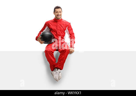 A piena lunghezza Ritratto di un corridore in un uniforme rosso seduto su un pannello tenendo un casco e sorridente isolati su sfondo bianco Foto Stock