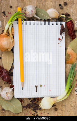 Notebook per scrivere ricette sullo sfondo di un tagliere con spezie Foto Stock