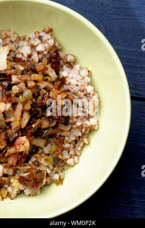 Deliziosa casa stufato di grano saraceno con pancetta arrosto, la cipolla, la carota e il peperone closeup nella ciotola verde su sfondo di legno. Vista superiore Foto Stock