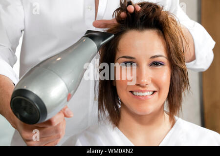 Vista ritagliata del parrucchiere donna di asciugatura dei capelli. Vista frontale Foto Stock