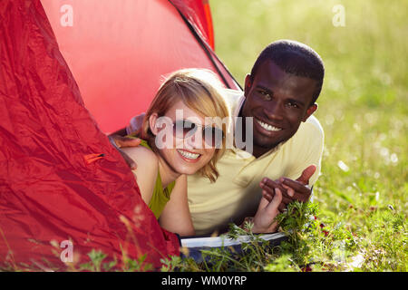 Giovane coppia multietnica giacente in tenda e tenendo le mani. Foto Stock