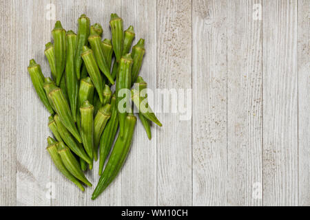 Fresco verde organico okra isolate su un legno bianco con bordo copia spazio. Foto Stock