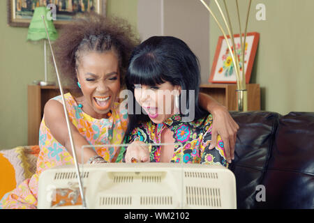 Coppia mista di amici ridere insieme nella parte anteriore del televisore Foto Stock