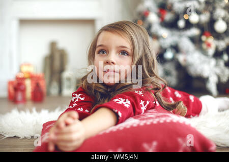 5 anni bambina recante sul morbido cuscino vicino albero di Natale a casa Foto Stock