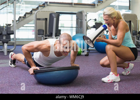 Vista di una femmina di trainer assiste l uomo con push ups in palestra Foto Stock