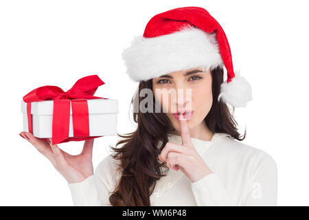 Festive brunette holding dono e mantenere un segreto su sfondo bianco Foto Stock