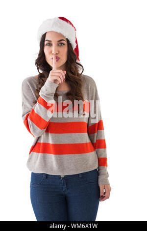 Festive brunette in santa hat mantenendo un segreto su sfondo bianco Foto Stock