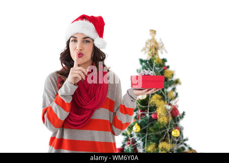 Festive brunette mantenere segreto e tenendo il dono per la struttura ad albero su sfondo bianco Foto Stock