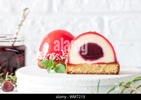 Mousse di moda la torta con la glassa a specchio e ciliegia riempimento su un cuscino di noci di cocco biscotti con scaglie di noce di cocco. Moderno e dessert. Foto Stock