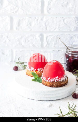 Mousse di moda la torta con la glassa a specchio e ciliegia riempimento su un cuscino di noci di cocco biscotti con scaglie di noce di cocco. Moderno e dessert. Foto Stock