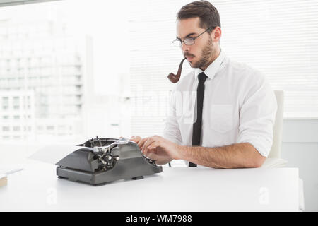 Hipster imprenditore utilizzando una macchina da scrivere di fumare un tubo nel suo ufficio Foto Stock