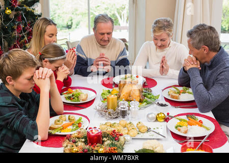 Famiglia estesa dicendo grazia prima di cena di Natale a casa nella sala da pranzo Foto Stock