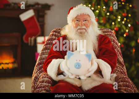 Sorridente santa offrendo salvadanaio a casa nel soggiorno Foto Stock