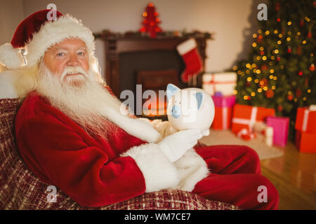 Santa Claus holding salvadanaio a casa nel soggiorno Foto Stock