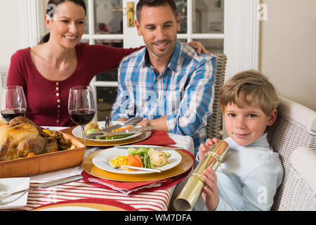 Carino figlio tenendo un christmas cracker a casa nel soggiorno Foto Stock