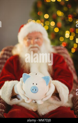 Santa Claus offrendo salvadanaio a casa nel soggiorno Foto Stock