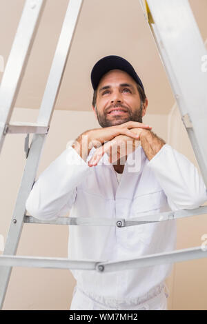 Pittore sorridente appoggiato su scala in una nuova casa Foto Stock