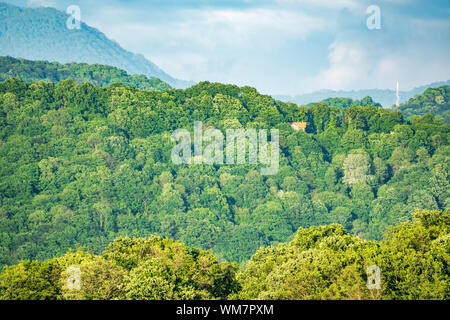 Verde collina con lonely house e di alta montagna all'orizzonte. Valle Verde con villaggi nella luce del tramonto. Foto Stock