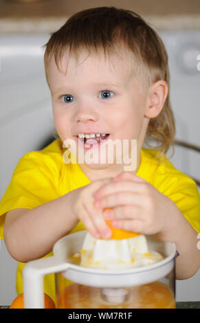 Il bambino in un giubbotto di colore giallo per strizzare fuori dal succo di un arancio Foto Stock