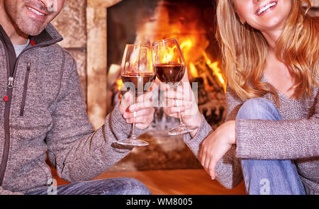 Felice coppia giovane seduto vicino al camino e bere il vino, romantiche data, celebra il giorno di San Valentino in un accogliente winter house Foto Stock