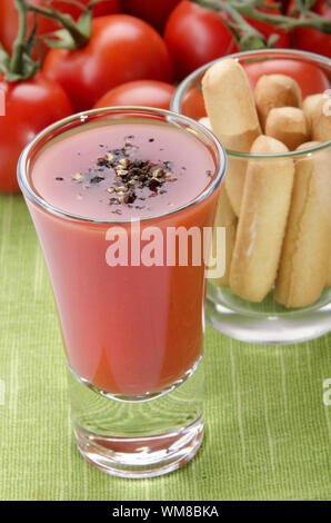 Bloody Mary cocktail con pepe macinato in un piccolo colpo di vetro, grissini e pomodoro fresco sul tavolo verde panno Foto Stock