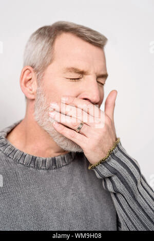 Senior collocando man mano sulla bocca sbadigli Foto Stock
