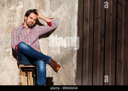 Sorridente modello maschile seduto sulla cassa di legno con le gambe incrociate Foto Stock