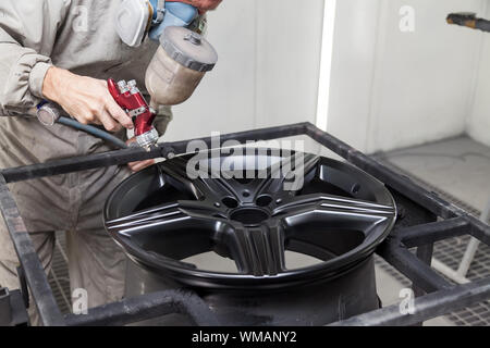 Verniciatura del corpo di elemento della vettura - la lega di alluminio ruota con l aiuto di aerograf in colore nero dalla mano del pittore repairman nell'indus Foto Stock