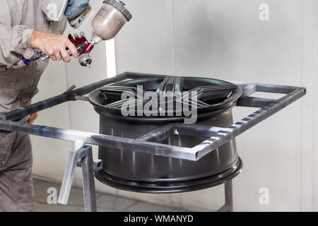 Verniciatura del corpo di elemento della vettura - la lega di alluminio ruota con l aiuto di aerograf in colore nero dalla mano del pittore repairman nell'indus Foto Stock