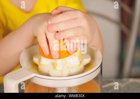 Il bambino in un giubbotto di colore giallo per strizzare fuori dal succo di un arancio Foto Stock