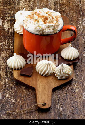 Meringhe e tazza di cioccolata calda con panna montata e cannella sul tagliere in legno rustico sfondo Foto Stock