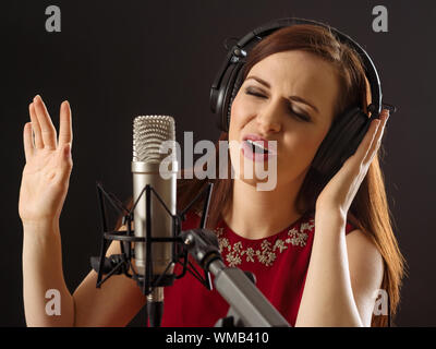 Foto di una bella donna cantare in un diaframma grande microfono su sfondo scuro. Foto Stock