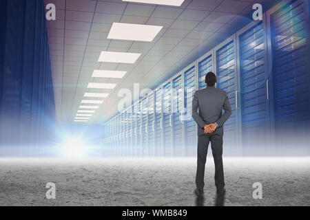 Giovane imprenditore in piedi con le mani dietro la schiena contro il corridoio del server in Impostazione del deserto Foto Stock