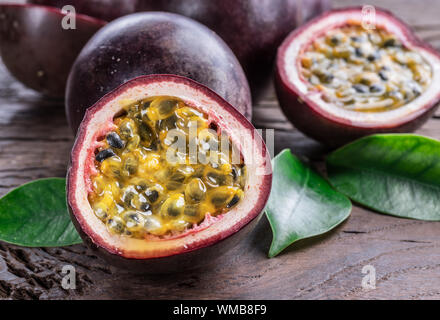 Frutti della passione e la sua sezione trasversale con succo di polpa riempito con semi. Sfondo di legno. Foto Stock