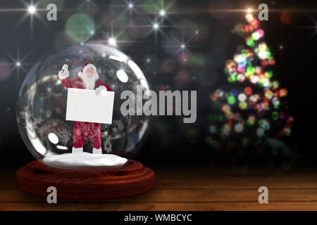 Santa squillo di campana e Holding firmano in snow globe contro luce scintillante disegno sulle commissioni Foto Stock