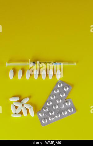 Una dispersione di bianco di forma ovale compresse e una siringa medica su sfondo giallo. Close-up. Foto Stock