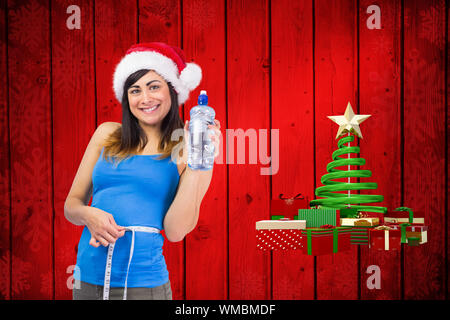 Montare festosa brunette misurando la sua vita e vaso di contenimento contro l albero di natale forma sul legno rosso Foto Stock