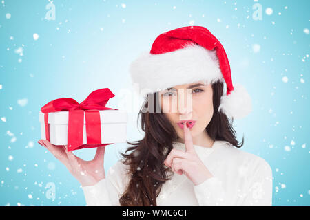 Festive brunette holding dono e mantenere un segreto contro il bollino blu Foto Stock