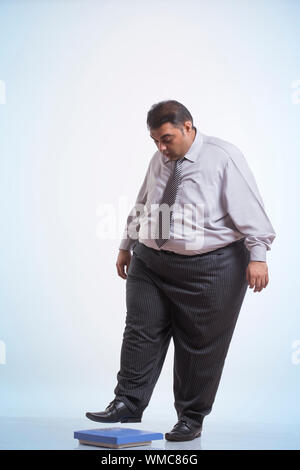 Obeso di indossare abiti formali stepping sulla macchina di pesatura Foto Stock