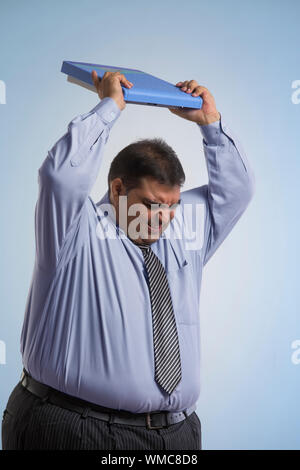 Frustrati obeso di indossare abiti formali il sollevamento di una bilancia di pesatura sopra la sua testa di lanciarla Foto Stock